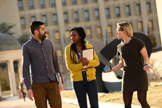 Three students walking in Kogan Plaza together holding books