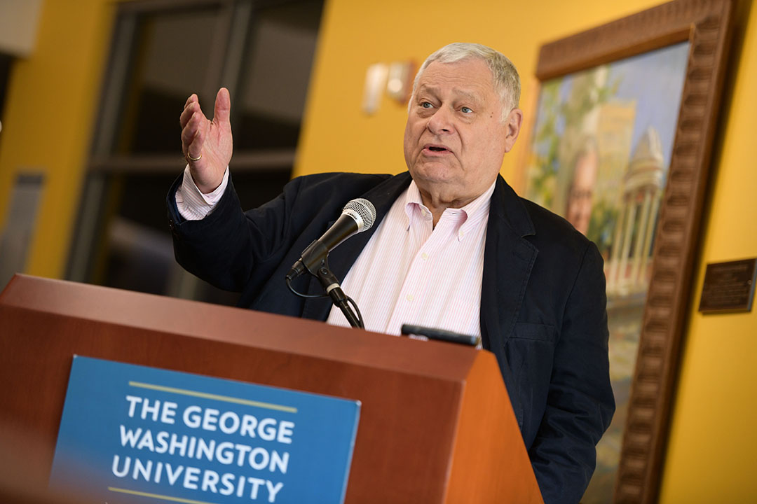 Stephen Joel Trachtenberg speaking at a podium decorated with a George Washington University sign