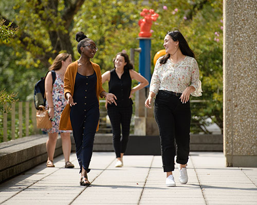 Group of students of mixed ethnicities walking outside around GW campus with leafy trees