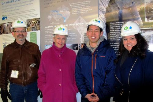 Two TSPPPA ENRP students and two older adults all wearing hard hats and standing in front of a DC Water sign