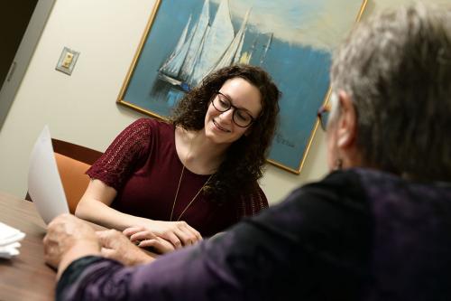 A woman student sitting at a desk across from a faculty member in a meeting