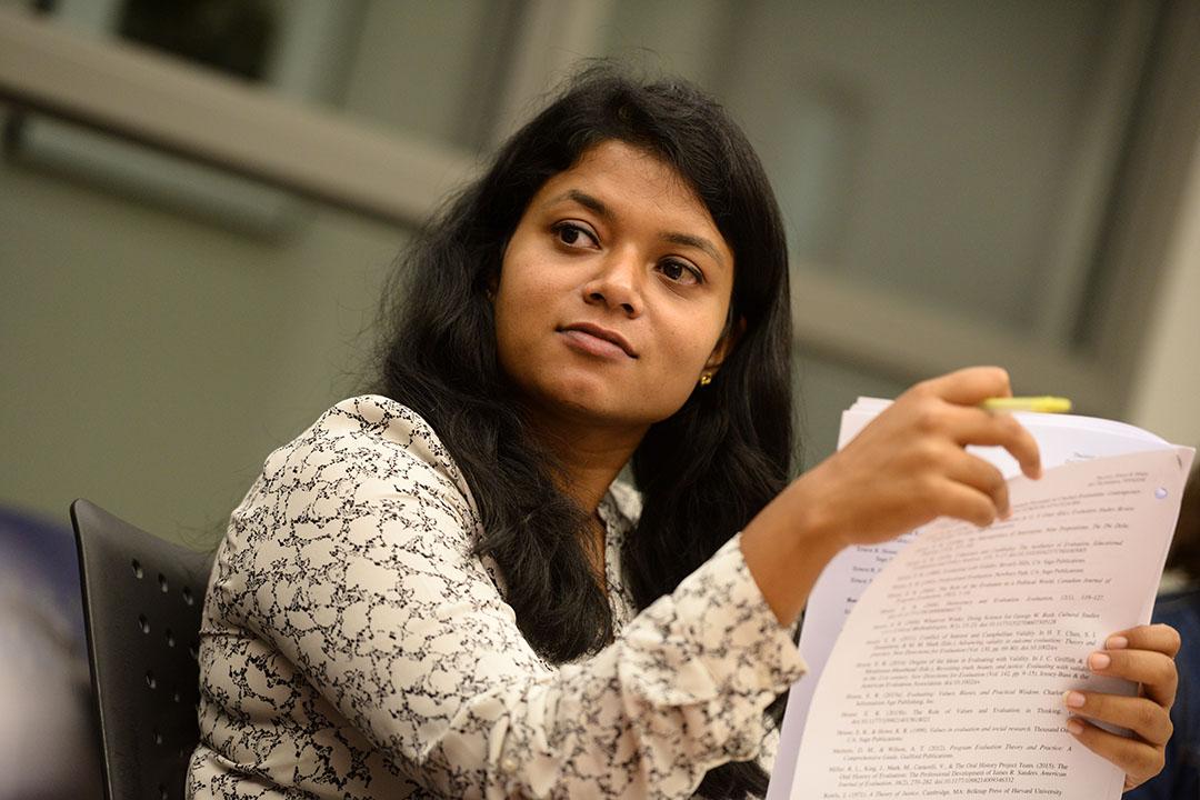 Image of a TSPPPA doctoral student with long hair at a desk chair holding a stack of papers and a highlighter