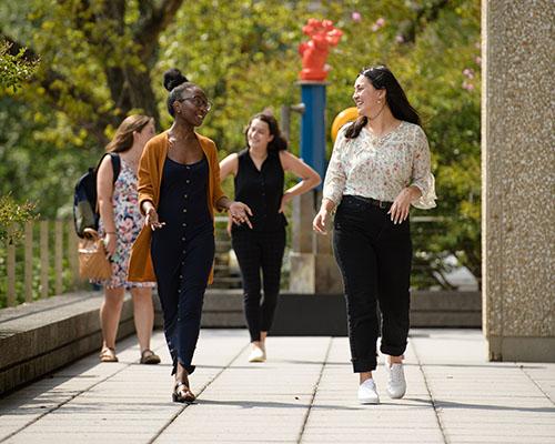 Group of students of mixed ethnicities walking outside around GW campus with leafy trees